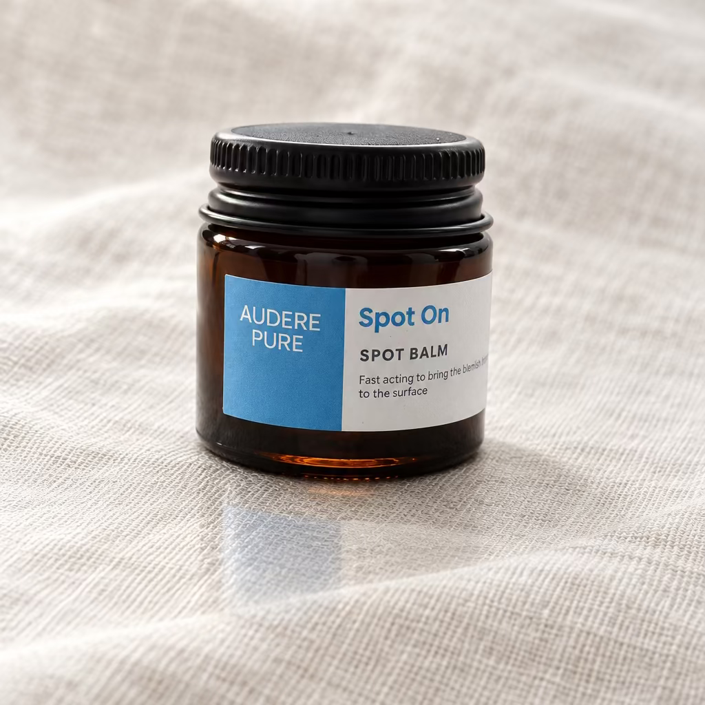A small amber glass jar of Audere Pure Spot On Spot Balm with a black lid and a blue and white label, sitting on a white surface.